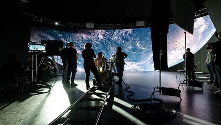 A film production crew standing in front of a large background screen as a systems-solution production setup.